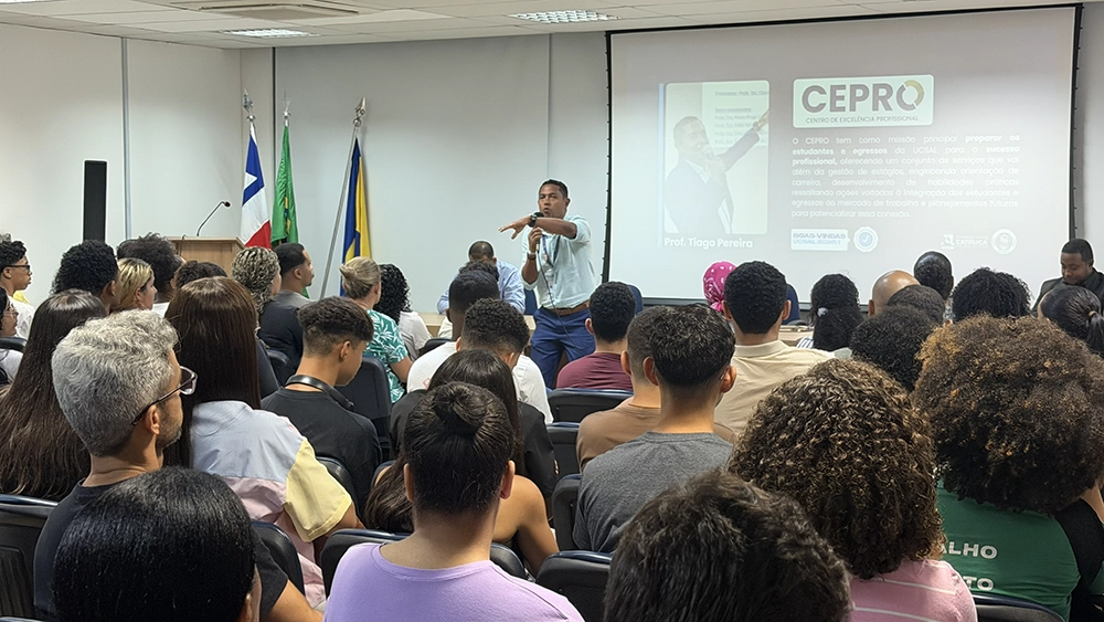 Auditório cheio de estudantes acompanhando uma apresentação do CEPRO, com o logotipo do Centro projetado ao fundo.